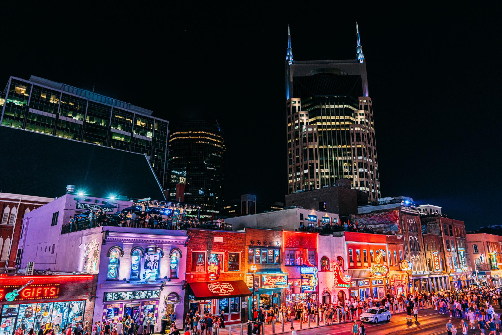 Crowds on Broadway in downtown Nashville at night with neon lights, bars, and live music venues attracting tourists