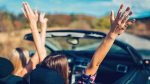 Friends enjoying a summer road trip in a convertible car representing the shift toward drivable vacation destinations in the U.S.