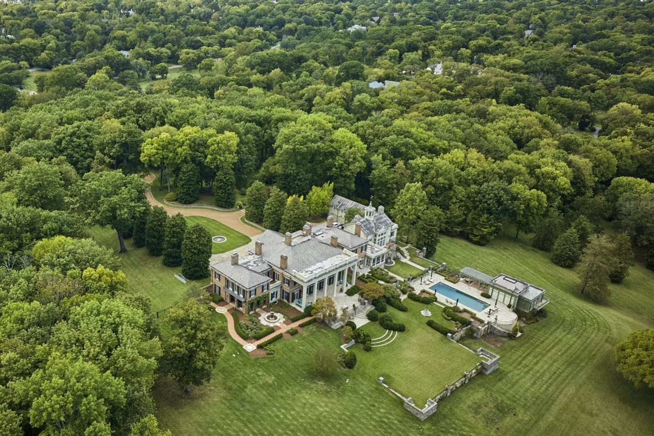 Aerial view of a columned limestone estate home in Belle Meade, Nashville, with a pool, formal gardens, and long tree-lined grounds
